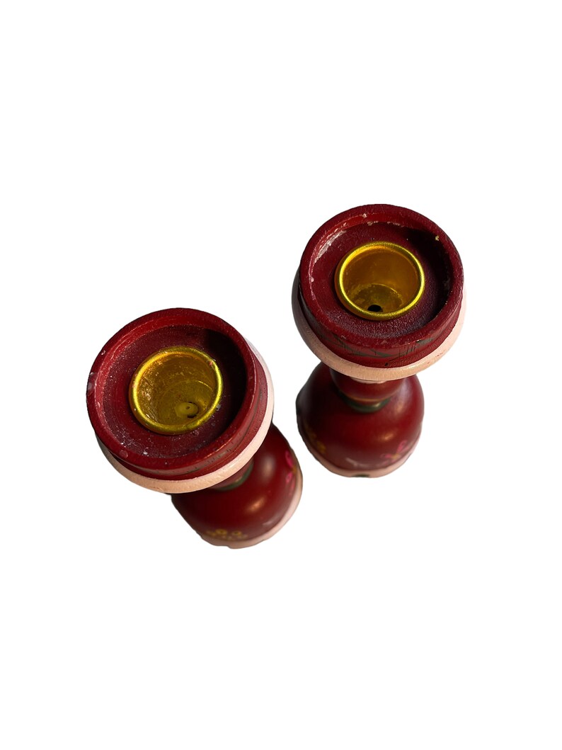 May include: Two red wooden candle holders with gold accents and floral designs. The candle holders are empty and ready to be used.