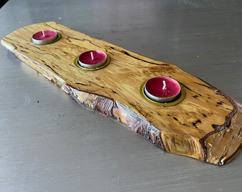 May include: A wooden candle holder with a natural wood finish and three tealight candle holders. The wood has a unique grain pattern and a rustic look.