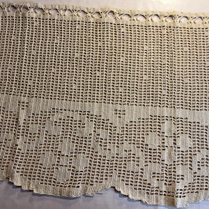May include: A beige, handmade crochet lace curtain panel. The top edge features a series of small, circular openings, while the bottom edge has a scalloped design. The open weave allows light to filter through, creating a delicate and airy aesthetic.