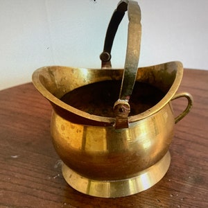 Könnte beinhalten: Ein kleiner, dekorativer Topf aus Messing mit einem Henkel. Der Topf hat einen runden Körper und einen ausgestellten Rand. Er hat einen kleinen Henkel an der Seite.