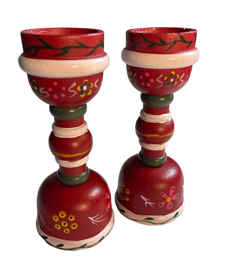 May include: A pair of red wooden candle holders with white and green painted details. The holders feature a floral design and are perfect for adding a touch of rustic charm to your home decor.