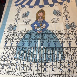 Puede incluir: Un paño de cocina decorativo vintage con una ilustración de dibujos animados de una mujer con un vestido azul sosteniendo flores. El diseño incluye un toldo a rayas azules y blancas, herrajes decorativos y pájaros azules sobre un fondo blanco con un borde azul.