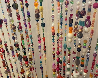 May include: A colorful beaded curtain with strands of various colors and textures, including glass, wood, and plastic beads. The curtain is made up of many different strands of beads, each with its own unique pattern and design.