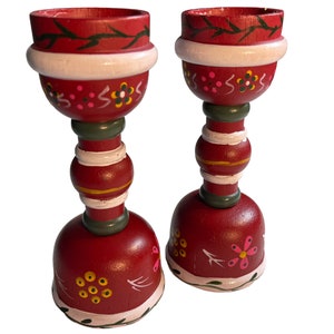 May include: A pair of red wooden candle holders with white and green painted details. The holders feature a floral design and are perfect for adding a touch of rustic charm to your home decor.