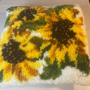 May include: A white, fluffy pillow with a colorful sunflower design. The sunflowers are yellow, brown, and green. The pillow is perfect for adding a touch of nature to any room.