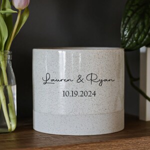 Könnte beinhalten: Weißer Keramiktopf mit gesprenkeltem Finish. Der Topf trägt den Text "Lauren & Ryan 10.19.2024".