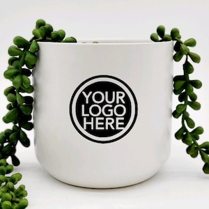 May include: White ceramic planter with a black circle that says "YOUR LOGO HERE" and a green succulent plant hanging over the side.