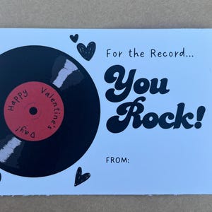 May include: A Valentine's Day card with a black vinyl record graphic and the words "For the Record... You Rock!" in black script. The record has a red center with "Happy Valentine's Day!" written on it. Small black hearts are scattered around the card.
