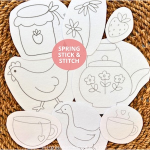 May include: A collection of white fabric patches with spring-themed line drawings, including a chicken, teapot, teacup, and strawberry. The text "Spring Stick & Stitch" is in a pink circle. The patches are arranged on a woven brown surface.