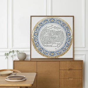 May include: A framed circular artwork with ornate blue and gold patterns and Hebrew text. The artwork is displayed on a wooden cabinet in a well-lit room. The artwork is the focal point of the room.