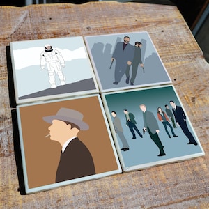May include: Set of four square ceramic coasters featuring minimalist illustrations. Designs include an astronaut, figures with guns, a man in a hat smoking, and a group of people in suits. Each coaster has a white border.
