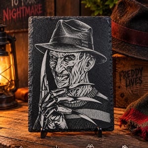May include: A rectangular black slate plaque featuring a laser-engraved illustration of a character wearing a fedora hat and a striped sweater, with sharp metal blades attached to the fingers of one hand, displayed on a small black stand.