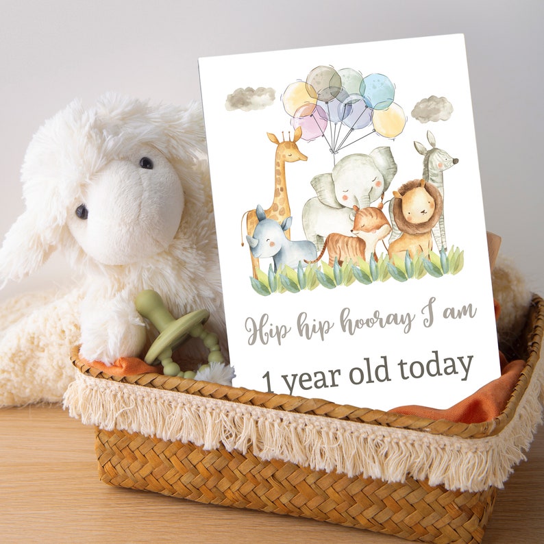 May include: A white card with a watercolor illustration of a giraffe, elephant, rhino, tiger, and lion. The animals are surrounded by green leaves and colorful balloons. The text on the card reads "Hip hip hooray I am 1 year old today".