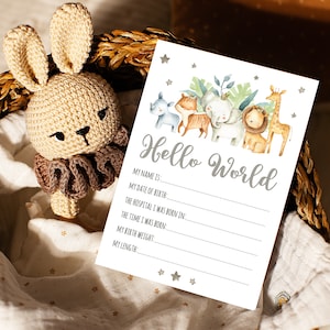May include: A white card with the text "Hello World" in gray lettering. The card has a line for the baby's name, date of birth, hospital, time of birth, birth weight, and length. The card is decorated with watercolor illustrations of animals, including a giraffe, lion, elephant, rhino, and tiger.