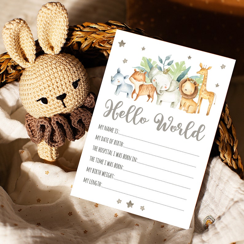 May include: A white card with the text "Hello World" in gray lettering. The card has a line for the baby's name, date of birth, hospital, time of birth, birth weight, and length. The card is decorated with watercolor illustrations of animals, including a giraffe, lion, elephant, rhino, and tiger.