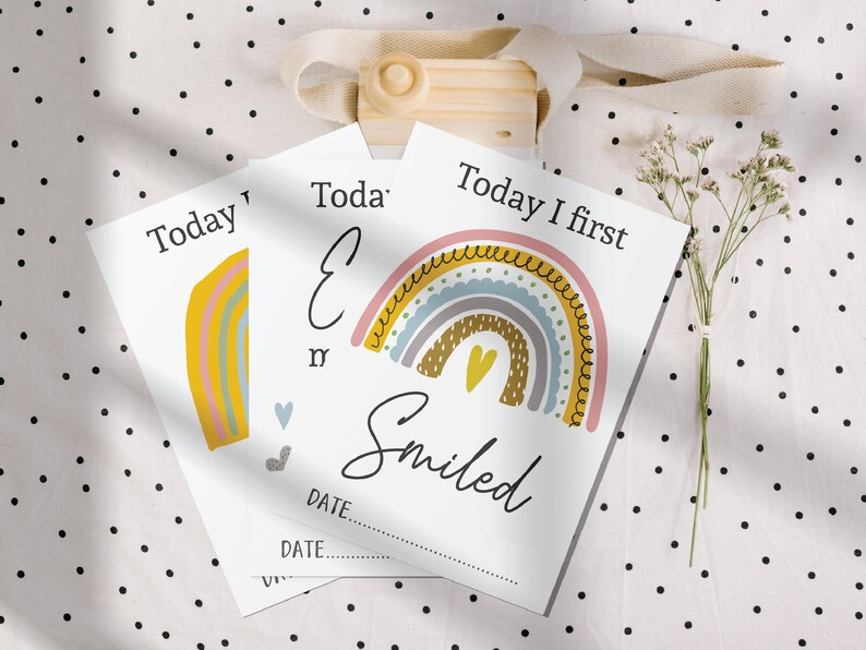 May include: A set of baby milestone cards featuring a rainbow design. Each card has a different milestone, such as "Today I first smiled". The cards are printed on white cardstock and have a simple, modern design.