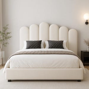 Puede incluir: Una cama tapizada de color crema con un cabecero arqueado único. La cama tiene un edredón blanco, un camino de cama marrón y dos almohadas acolchadas de color gris oscuro. Una mesita de noche negra y una lámpara decorativa son visibles en el fondo.