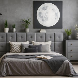 Könnte beinhalten: Ein modernes Schlafzimmer in Grautönen. Das Bett hat ein gepolstertes Kopfteil, graue Bettwäsche und Kissen. Ein großes Mondgemälde hängt an der Wand. Topfpflanzen und eine graue Kommode sind ebenfalls vorhanden.