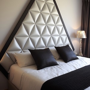 May include: A modern bed with a geometric headboard. The headboard is a large triangle with a dark wood frame and a white, quilted, diamond pattern. The bed has white sheets, black pillows, and a black throw blanket.