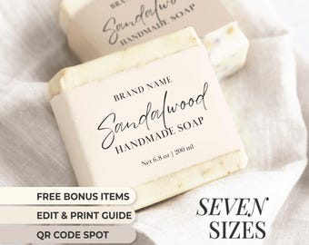 May include: A white bar of sandalwood soap with a pink label that reads "BRAND NAME Sandalwood HANDMADE SOAP Net 6.8 oz | 200 ml". The soap is sitting on a white fabric background. The image also includes text that reads "FREE BONUS ITEMS EDIT & PRINT GUIDE QR CODE SPOT SEVEN SIZES".