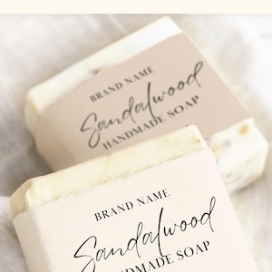May include: Two white bars of handmade sandalwood soap with beige labels. The labels have the text "BRAND NAME Sandalwood HANDMADE SOAP" and "Net 6.8 oz | 200 ml".