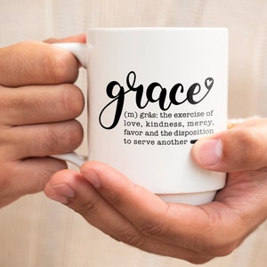 May include: White ceramic coffee mug with black text that reads "grace (m) gr&auml;s: the exercise of love, kindness, mercy, favor and the disposition to serve another".