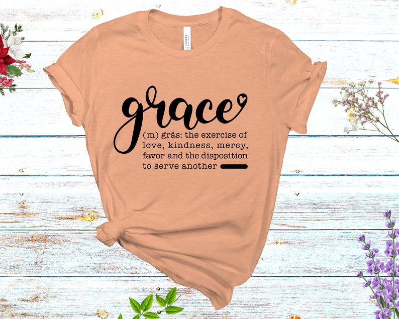 May include: A peach-colored t-shirt with the word "grace" in black cursive lettering. The word is defined as "the exercise of love, kindness, mercy, favor and the disposition to serve another".