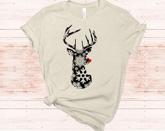 May include: A beige t-shirt with a black reindeer silhouette made of snowflakes. The reindeer has a red nose.