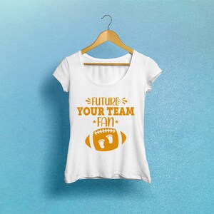 Puede incluir: Camiseta blanca con un gr&aacute;fico de f&uacute;tbol americano marr&oacute;n y el texto "FUTURE YOUR TEAM FAN" con una estrella a cada lado de la palabra "FAN".