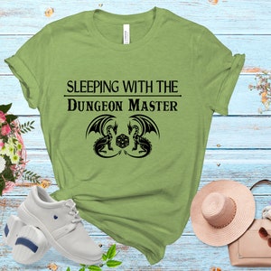 May include: Green t-shirt with the text "Sleeping with the Dungeon Master" and a black graphic of two dragons facing each other with a dice in the middle.