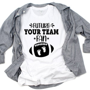 Puede incluir: Camiseta blanca con texto negro que dice "Future Your Team Fan" con un gr&aacute;fico de f&uacute;tbol negro con dos huellas dentro.