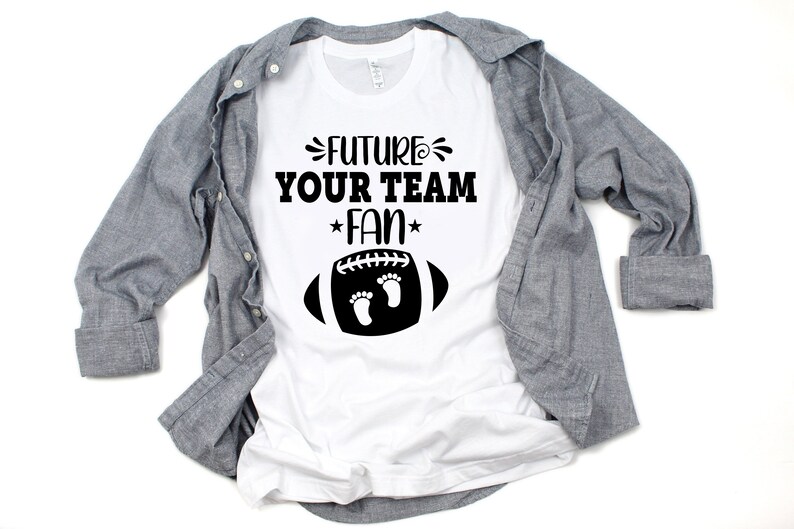 Puede incluir: Camiseta blanca con texto negro que dice "Future Your Team Fan" con un gr&aacute;fico de f&uacute;tbol negro con dos huellas dentro.