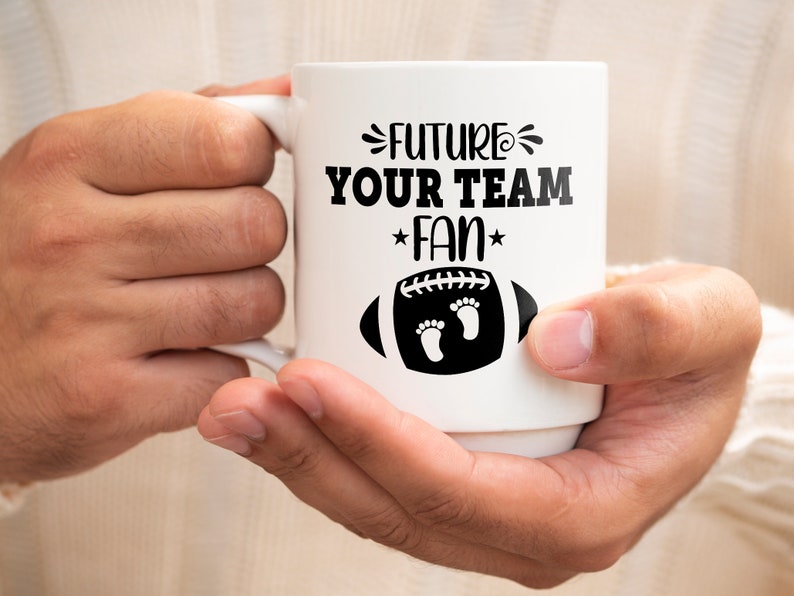 Puede incluir: Taza de cer&aacute;mica blanca con un dise&ntilde;o negro que dice "Future Your Team Fan" con un bal&oacute;n de f&uacute;tbol y huellas.