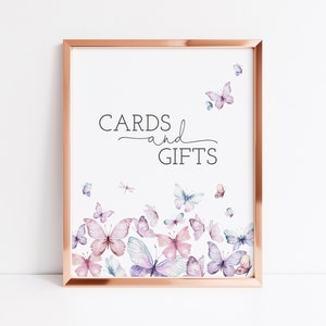 May include: A printable sign with a rose gold frame and the text "CARDS and GIFTS" in black. The background is white with a watercolor design of butterflies in shades of pink, purple, and blue.