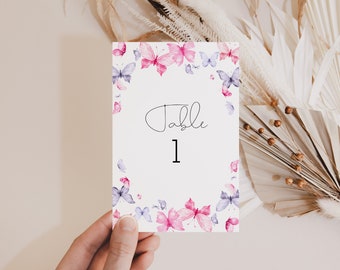 May include: A white card with a pink and purple butterfly border. The card says "Table 1" in black script.