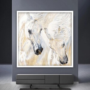 Op de afbeelding: Een schilderij van twee witte paarden met stromende manen, hun hoofden naar elkaar gekeerd. De achtergrond is een zachte, gouden kleur.