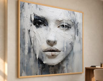 May include: A large rectangular wall art piece featuring a textured oil painting of a human face in shades of white, gray, and black. The artwork displays thick, impasto paint strokes with visible drips and a light wooden frame.