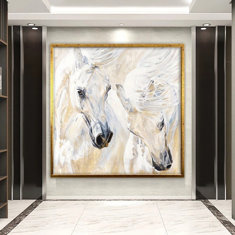 Op de afbeelding: Een schilderij van twee witte paarden met stromende manen, hun hoofden dicht bij elkaar. Het schilderij is ingelijst in goud en heeft een lichte achtergrond.