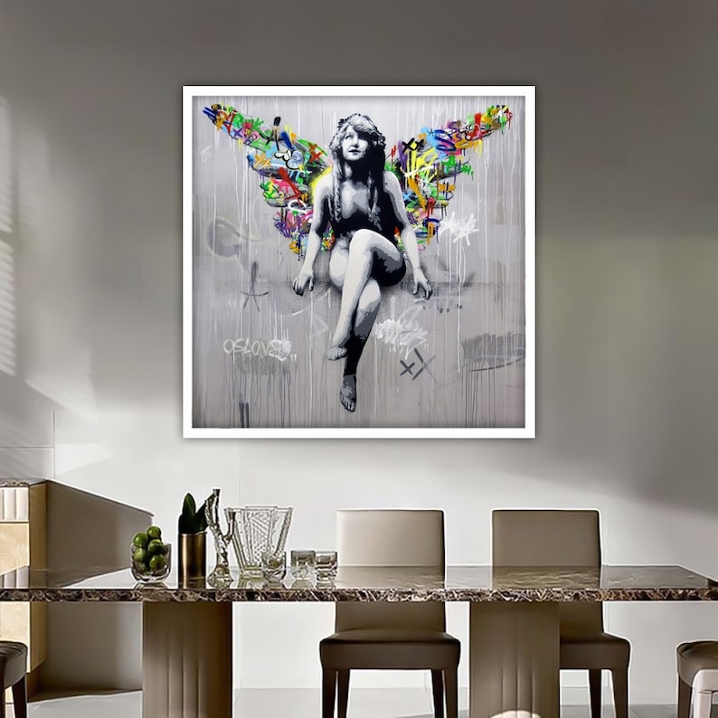 May include: A framed print of a woman with wings, sitting on a gray background with colorful graffiti. The woman is wearing a white dress and has long, dark hair. The graffiti includes the word "of love".