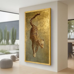 Puede incluir: Una obra de arte vertical enmarcada que presenta un leopardo con pelaje manchado sobre un fondo dorado. El leopardo está representado en una pose dinámica, con el cuerpo inclinado hacia abajo. El marco es de color dorado.
