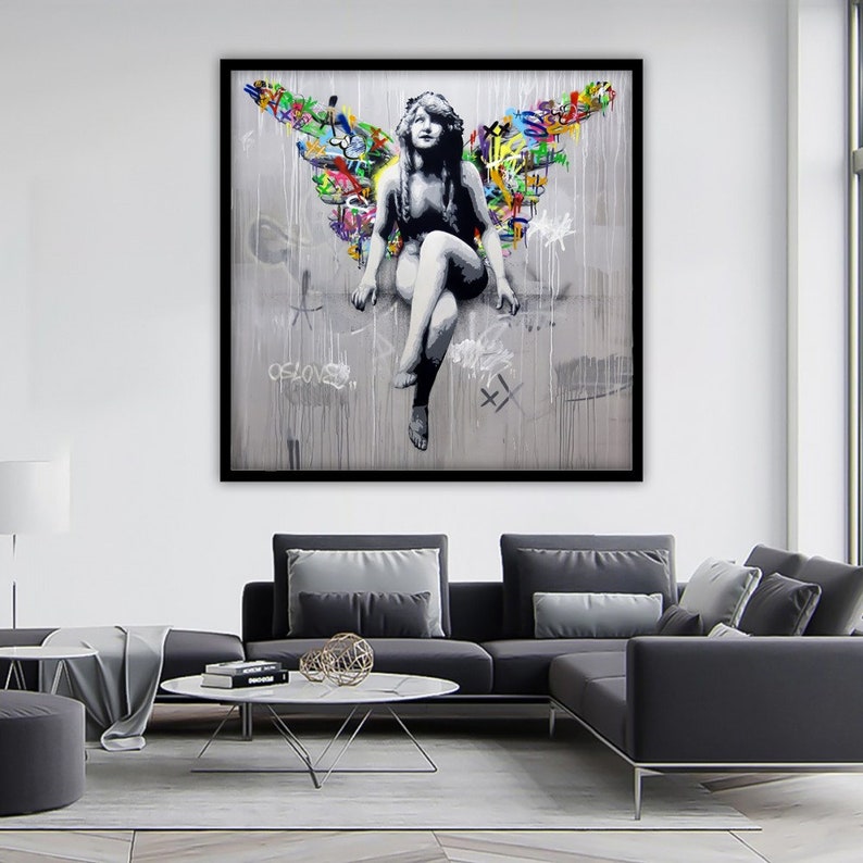 May include: A black and white image of a woman with wings made of colorful graffiti. The woman is sitting on a ledge with her legs crossed. The background is a gray wall with drips of paint.