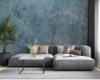 Könnte beinhalten: Ein graues Ecksofa mit verschiedenen Kissen steht vor einer blauen, strukturierten Wand. Ein kleiner Couchtisch mit einer weißen Marmorplatte steht vor dem Sofa. Eine Topfpalme steht in der Ecke des Raumes.