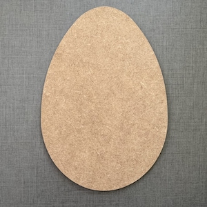 May include: A large, unfinished wooden egg shape, suitable for crafting or decoration. The egg is a light brown colour and rests on a grey textured surface. Ideal for Easter or spring projects.
