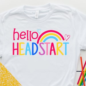 May include: White t-shirt with a rainbow and the text "hello headstart" in colorful letters.