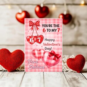 May include: A Valentine's Day card with the text "You're the 6 to my 7" and "Happy Valentine's Day!" is displayed. The card features red and pink hearts and a bow. Two knitted red hearts are on the sides.