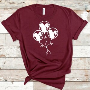 May include: A maroon t-shirt with a white graphic of three Mickey Mouse head balloons.