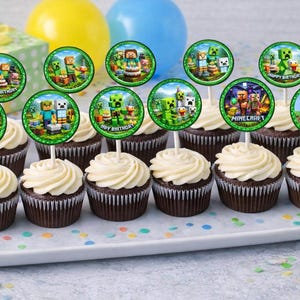May include: A tray of cupcakes with white frosting and round toppers featuring Minecraft characters and the words "Happy Birthday" and "Minecraft". The cupcakes are on a white tray, with colorful confetti scattered around.