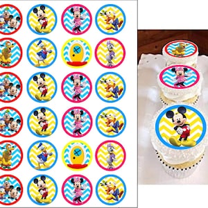 May include: A collection of colorful, circular cupcake toppers featuring Disney characters like Mickey Mouse, Minnie Mouse, Donald Duck, and Pluto. The toppers have a blue, red, or pink border with a yellow and white zigzag pattern. Some cupcakes are decorated with the same toppers.