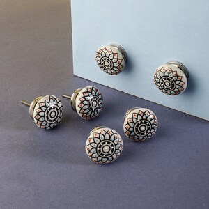 May include: Six white ceramic cabinet knobs with a silver base. Each knob features a black and white mandala design with red and blue accents.