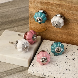 May include: Assortment of ceramic cabinet knobs in various colors, including white, pink, and teal. Each knob features a decorative floral design and a silver metal base.
